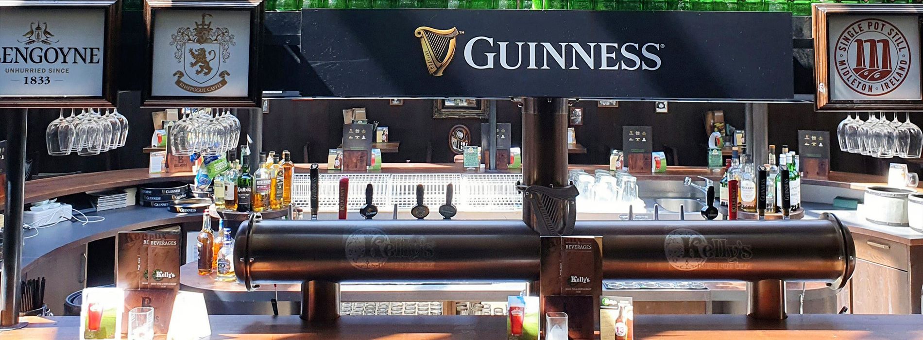 Barbereich mit Guinness-Zapfanlage, Spirituosenflaschen, Gläsern und dunkler Holztheke.