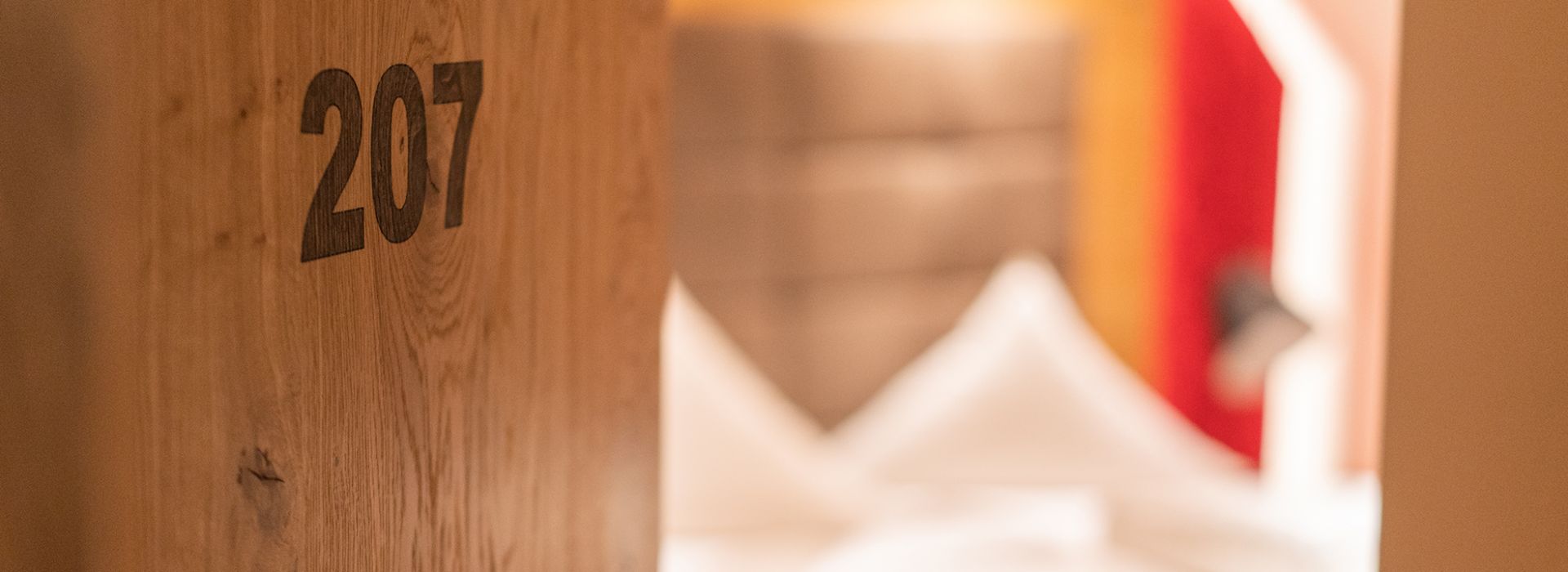 Zimmertür mit der Nummer 207 und Hotelzimmer im Hintergrund.