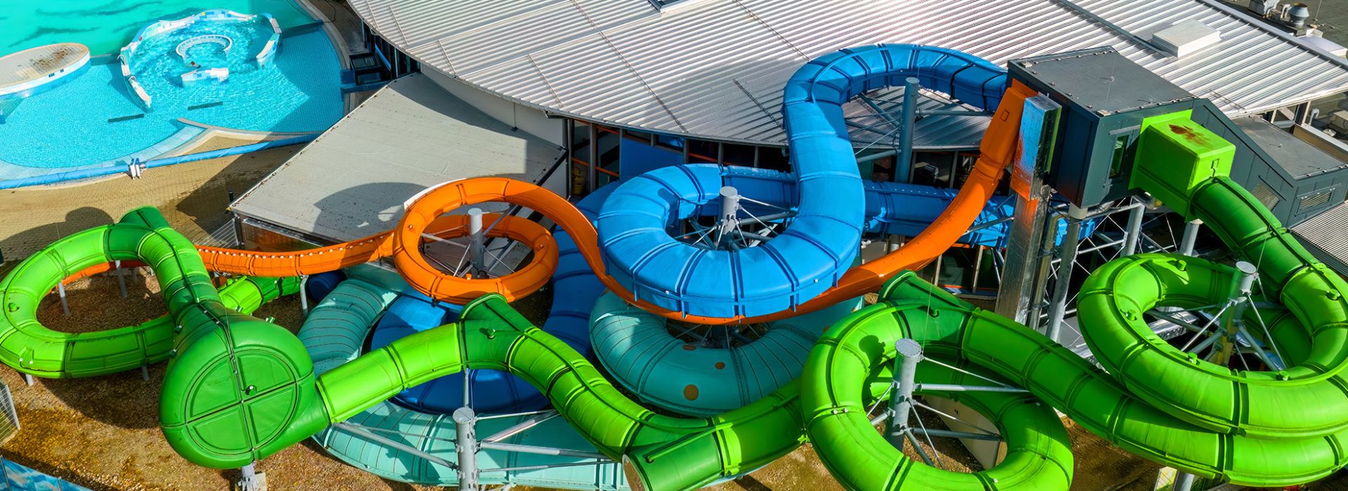 Luftaufnahme von verschlungenen Wasserrutschen in verschiedenen Farben auf Badeanlagendach.