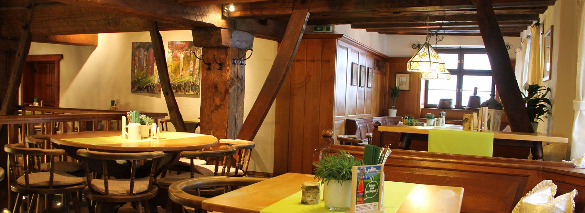 Gemütlicher Gastraum mit Holzbalken, rustikalen Tischen und grüner Tischdekoration in traditionellem Ambiente.