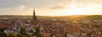 Stimmungsvolle Luftaufnahme der Stadt Ulm mit dem Ulmer Münster und roten Dächern im warmen Licht des Sonnenuntergangs.