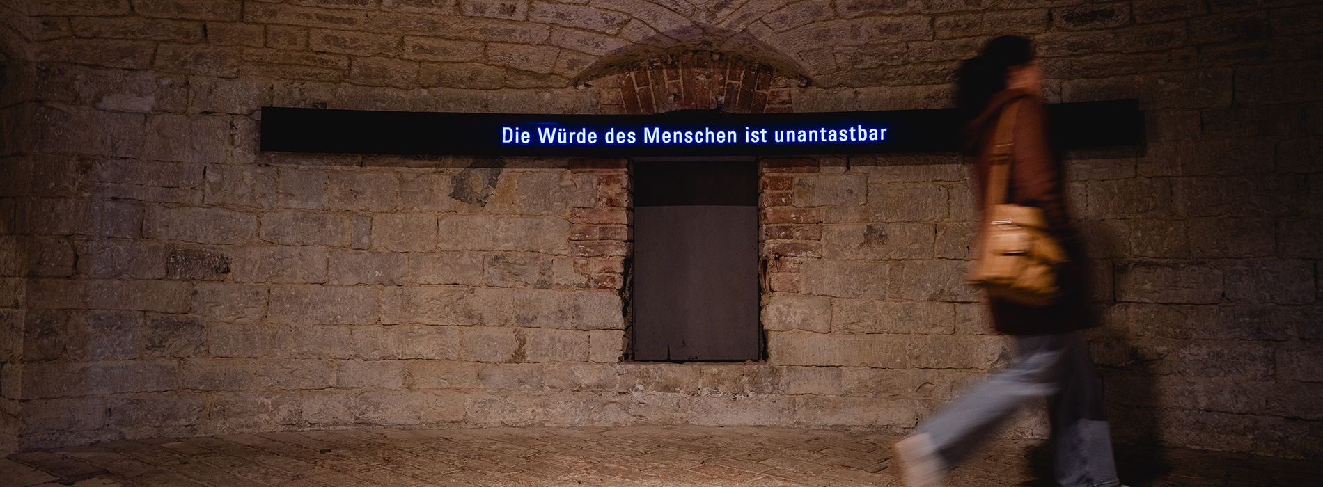 Gewölbter Museumsraum mit Ausstellungstafeln und mehreren Besucherinnen.
