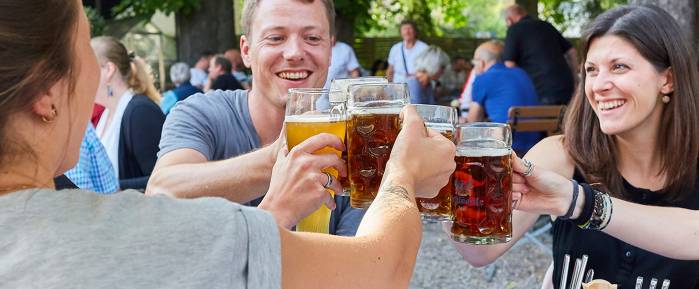 Menschen stoßen mit Bierkrügen im Biergarten an