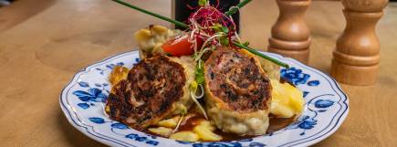 Ein traditionelles schwäbisches Gericht mit knusprig angebratenen Maultaschen auf Kartoffelsalat, garniert mit frischen Kräutern und Gemüse auf einem blauen Porzellanteller.