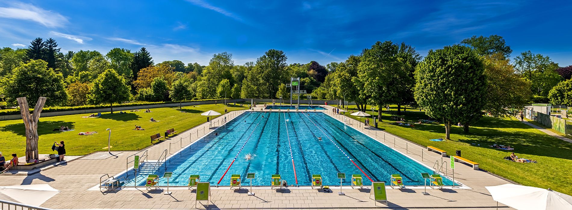 Schwimmerbecken mit markierten Bahnen in Freibadanlage umgeben von grüner Wiese.